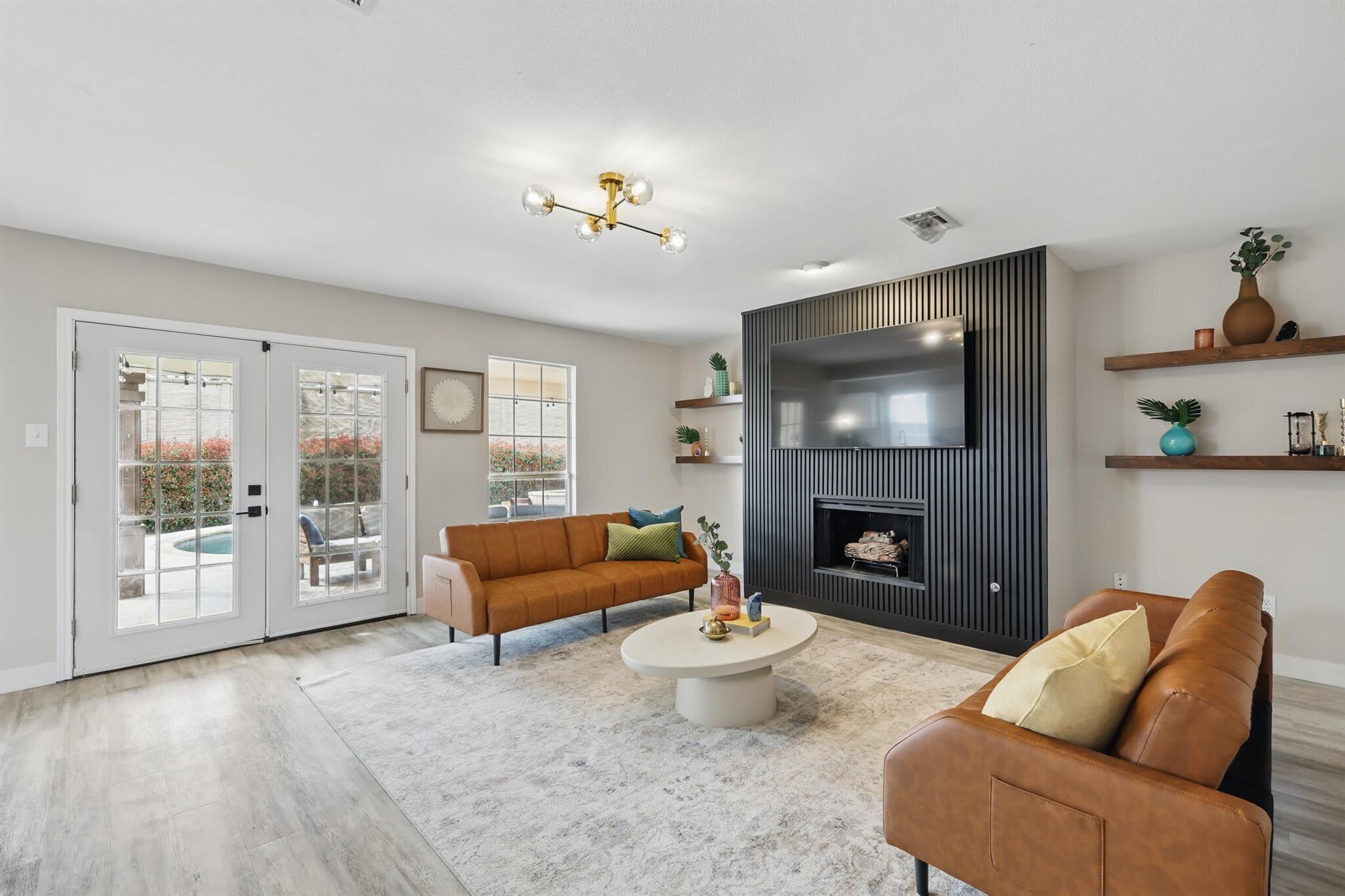 A living room with a sofa, coffee table, TV, fireplace, and sliding glass doors leading to a pool.