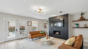 A living room with a sofa, coffee table, TV, fireplace, and sliding glass doors leading to a pool. - 4-bd/2.5-ba Tropical Pool Oasis With a Game Room (Flower Mound)