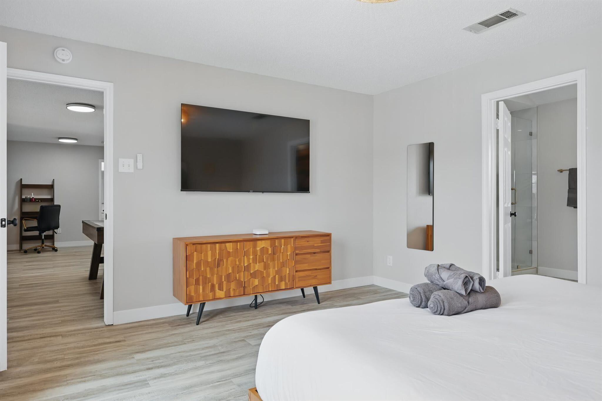 A bedroom with a bed, a wooden dresser, a flat-screen TV, and a walk-in closet.