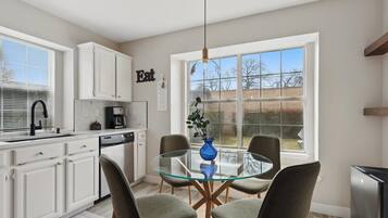 A modern kitchen with white cabinets, a glass dining table, and a view of the outdoors.
