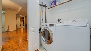A laundry room with a washing machine and dryer, wooden flooring, a chair, and a shelf with cleaning supplies. - 3 Bedrooms, Spacious Central Condo w Pool (Houston)