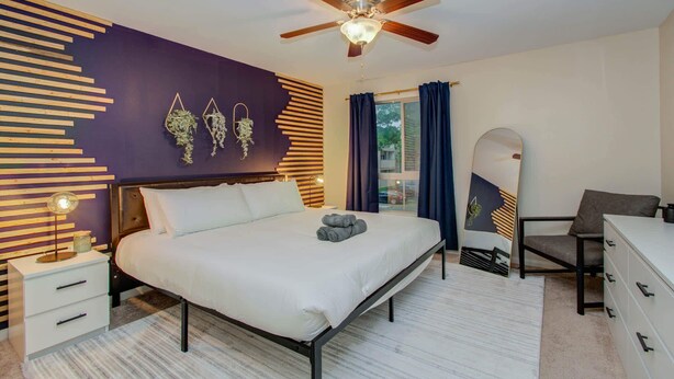 A modern bedroom with a bed, bedside tables, a ceiling fan, and a window with curtains. - 3 Bedrooms, Spacious Central Condo w Pool (Houston)