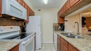 A kitchen with granite countertops, a stove, a refrigerator, wooden cabinets, and a built-in microwave. - 3 Bedrooms, Spacious Central Condo w Pool (Houston)