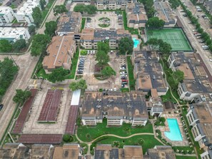 Ein Luftbild eines Wohngebiets mit mehreren Gebäuden, einem Tennisplatz und einem Schwimmbad.