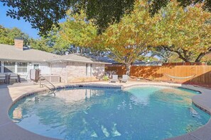 Ein Pool mit geschwungener Kante, ein Holzzaun und ein Baum mit Herbstlaub.