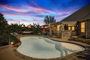 Una piscina con cubierta de piedra, un área de estar techada y una casa con fachada de piedra.