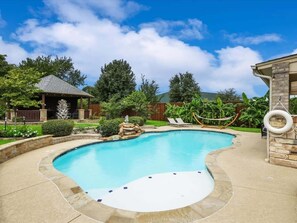 Une piscine à bord incurvé, entourée d’une terrasse en pierre, et agrémentée d’une petite cascade.