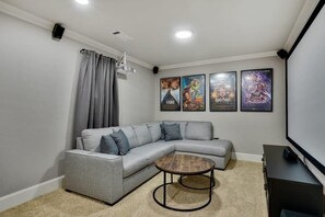 Un salon moderne avec un canapé d’angle gris, une table basse ronde et un téléviseur à écran plat.