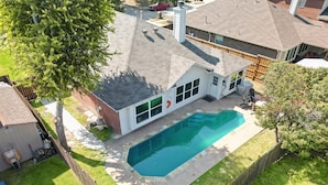 Una propiedad residencial con piscina, un patio cercado y una casa con techo inclinado.