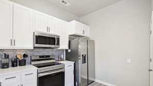 Una cocina con armarios blancos, electrodomésticos de acero inoxidable y un revoque de azulejos.