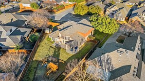 Vista aérea de un barrio residencial con casas, árboles y un parque infantil.