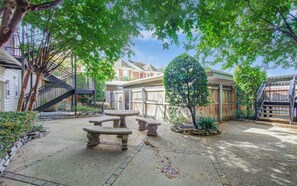 Un jardin avec une table en pierre, une clôture en bois et un escalier menant à une maison.