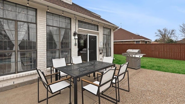 Eine Terrasse mit Tisch und Stühlen, einem Grill und einem überdachten Bereich mit Fenstern.