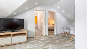A modern loft bedroom with a sloped ceiling, a TV on a wooden cabinet, a bed, and a desk with chairs. - Gorgeous home in Gospic with sauna (Gospic)