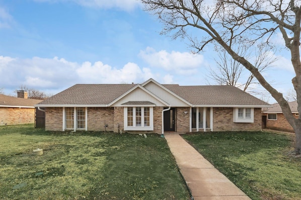 A single-story brick house with a front porch, a driveway, and a tree in the yard. - Best of Desoto 4br,3ba With Pool, Hottub, Cinema (DeSoto)