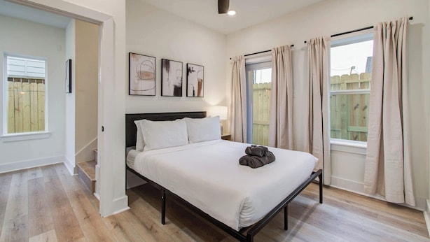 Une chambre à coucher avec un lit, un ventilateur de plafond, des œuvres d’art et une vue sur une clôture en bois.