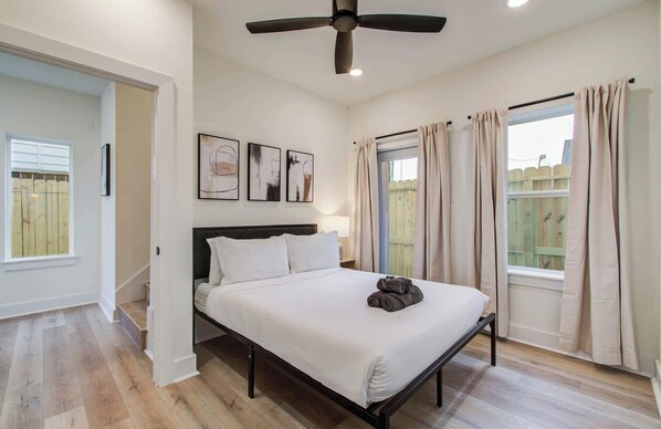 A bedroom with a bed, ceiling fan, artwork, and a view of a wooden fence. - Chic & Central 3BD Townhouse, Mins to DT & Midtown (Houston)