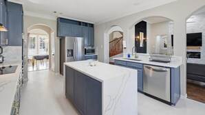 A modern kitchen with a central island, built-in appliances, and a dining area with natural light. - 6BD Luxury Retreat w Backyard & Access Golf Course (Frisco)
