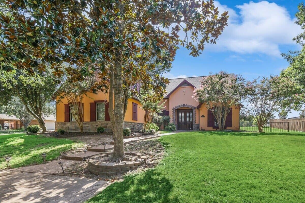A two-story house with a stone foundation and a yellow facade, surrounded by a well-maintained lawn and mature trees.