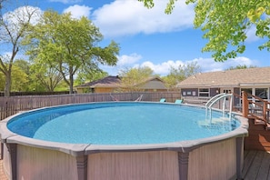 Ein oberirdischer Swimmingpool mit Holzterrasse, umgeben von Holzzaun und Bäumen.