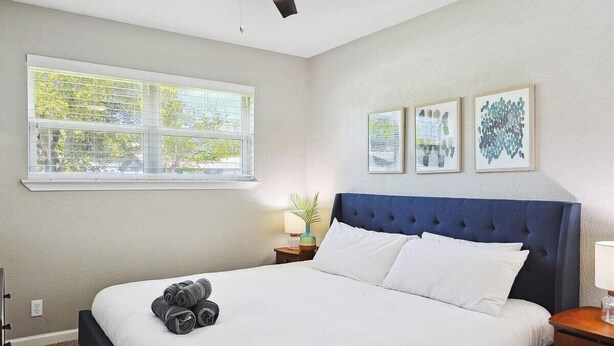 A hotel room with a large bed, a ceiling fan, a window with blinds, and three framed artworks on the wall. - 4-bd Luxury Retreat Pool, Grill, Outdoor cinema (Richardson)