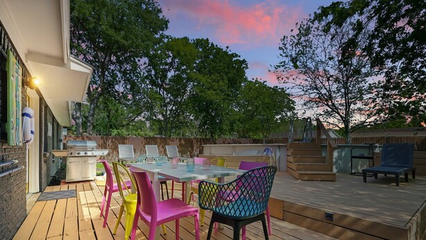 Un patio al aire libre con una mesa, sillas, una parrilla y una terraza de madera.