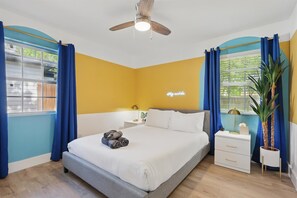 Ein Schlafzimmer mit Bett, Nachttisch, Deckenventilator und einem Fenster mit Vorhängen.