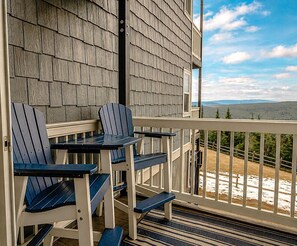 Eine Holzterrasse mit Adirondack-Stühlen und Blick auf eine bewaldete Landschaft.