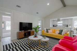 A modern living room with a yellow sofa, a flat-screen TV, and a black and white striped rug. - Vibrant Spacious Home w/ Private Pool and Jacuzzi (Richardson)
