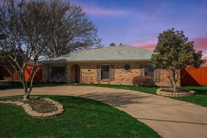 A single-story brick house with a front entrance, a covered porch, and a well-maintained lawn. - Vibrant Spacious Home w/ Private Pool and Jacuzzi (Richardson)