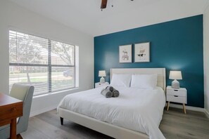 A bedroom with a large bed, two bedside tables with lamps, a window with blinds, and artwork on the wall. - Vibrant Spacious Home w/ Private Pool and Jacuzzi (Richardson)