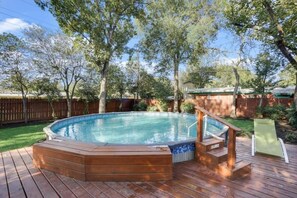 Un jacuzzi en una terraza de madera con una piscina al fondo.