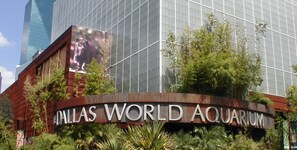 Fasaden på Dallas World Aquarium med en stor skylt och en byggnad med glasfasad i bakgrunden.