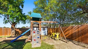 Une aire de jeux avec un toboggan, un mur d’escalade et des balançoires.