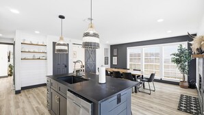 Une cuisine moderne dotée d’un îlot central, d’appareils électroménagers en acier inoxydable, de luminaires suspendus et d’un coin repas avec une table et des chaises.