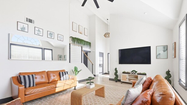 Un salon spacieux avec un grand canapé, une table basse et un téléviseur. On y trouve un escalier agrémenté d’une rambarde où sont posées des plantes, et les murs sont décorés de tableaux encadrés.