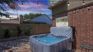 A hot tub in a backyard with a brick wall, wooden fence, and string lights. - Luxury 5BR Getaway w/ Pool, Hot Tub & cinema (DeSoto)