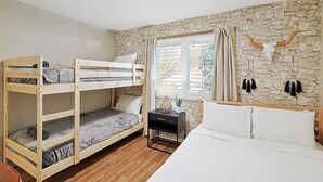 A room with bunk beds, a single bed, a nightstand, a potted plant, and a stone wall. - Luxury 5BR Getaway w/ Pool, Hot Tub & cinema (DeSoto)