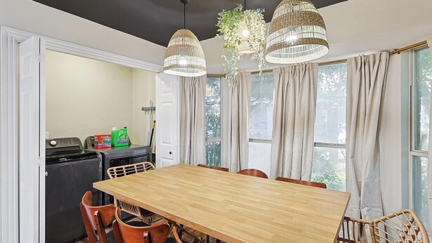 A dining area with a wooden table and chairs, a black appliance, and a window with curtains. - Luxury 5BR Getaway w/ Pool, Hot Tub & cinema (DeSoto)