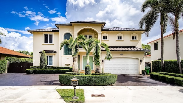 A two-story house with a garage, a well-maintained lawn, and a street lamp. - Luxury Tropical Living - 4BR w Backyard Pool Oasis (Miami Lakes)