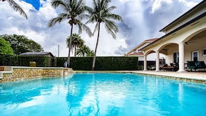 A swimming pool with palm trees and a covered patio area. - Luxury Tropical Living - 4BR w Backyard Pool Oasis (Miami Lakes)