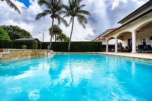 A swimming pool with palm trees and a covered patio area. - Luxury Tropical Living - 4BR w Backyard Pool Oasis (Miami Lakes)