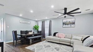 Ein modernes Wohnzimmer mit Essbereich, Deckenventilator und großem Fenster mit Vorhängen.