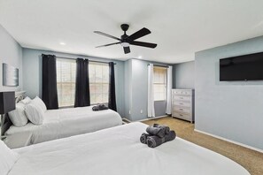 A hotel room with two beds, a ceiling fan, a TV, and a dresser. - 4 Bedrooms, Brick Retreat With Gameroom & Backyard (Grand Prairie)