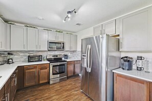 A modern kitchen with white cabinets, stainless steel appliances, and a wooden floor. - 4 Bedrooms, Brick Retreat With Gameroom & Backyard (Grand Prairie)