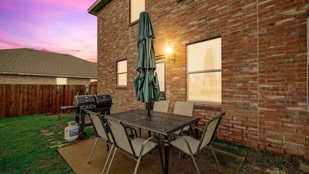 Ein Garten mit einer Ziegelhausfassade, einem Grill, einem Tisch mit Stühlen und einem Sonnenschirm.