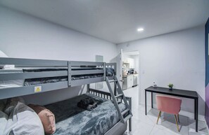 Ein Stockbett mit Schreibtisch und Stuhl, eine kleine Küche und ein durch eine geöffnete Tür einsehbares Badezimmer.
