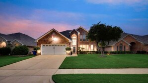 A two-story house with a garage, well-maintained lawn, and a driveway leading to the entrance. - Modern and Luxury DFW Mansion With Backyard Oasis (Fort Worth)
