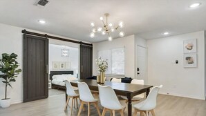 A modern dining area with a large table, white chairs, and a chandelier. - Luxury 4bed/2bath Hidden Gem w/ Backyard Oasis (North Richland Hills)