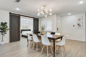 A dining area with a wooden table, white chairs, a chandelier, and a sliding barn door. - Luxury 4bed/2bath Hidden Gem w/ Backyard Oasis (North Richland Hills)